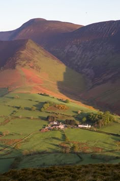 a green field with mountains in the background and a house on the other side that is surrounded by grass