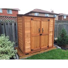 a wooden storage shed sitting in the middle of a yard next to a fence and bushes