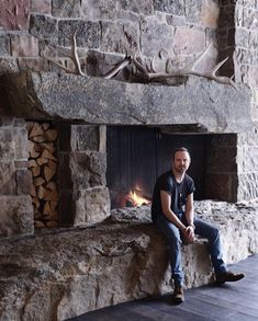 a man sitting in front of a stone fireplace