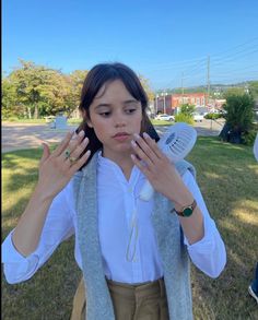 a woman in white shirt and tan pants holding her hands up to her face while standing on grass