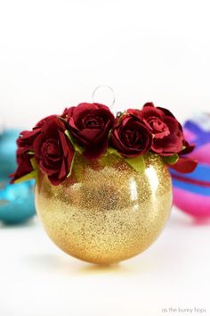 a gold vase filled with red roses on top of a white table next to ornaments