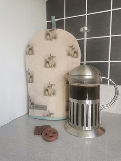 an oven mitt next to a coffee pot on a kitchen counter with donuts