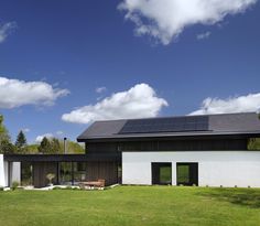 a house with a solar panel on the roof and grass in front of it, surrounded by trees