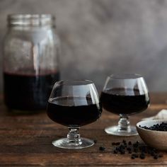 two wine glasses filled with red wine next to some black seeds on a wooden table