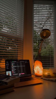 a laptop computer sitting on top of a wooden desk next to a window covered in blinds