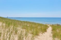 a path leading to the beach with grass on both sides and water in the background