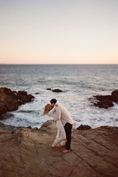 a man and woman are kissing on the rocks by the ocean at sunset or sunrise