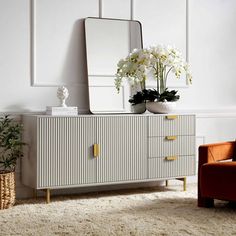 a living room with a chair, mirror and flowers on the sideboard in front of it