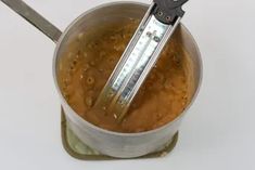 a measuring cup filled with brown liquid and topped with a large metal ladle that has a digital thermometer in it