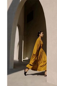 a woman in a yellow dress is walking through an archway with her hand on her hip