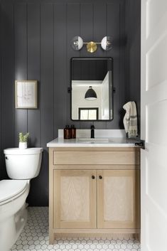 a white toilet sitting next to a bathroom sink under a mirror on top of a wooden cabinet