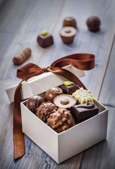 a white box filled with assorted chocolates on top of a wooden table next to other candies