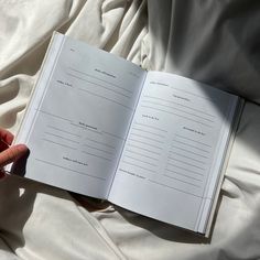 a person is holding an open book in their hand on a bed with white sheets