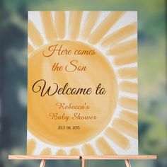 a welcome sign for a baby shower is displayed on a easel in front of a blurry background