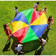 several children are playing with a large kite in the grass while adults watch from above