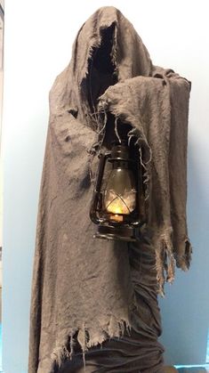 an old cloth draped around a lantern in the shape of a hooded up person's head