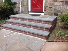 steps leading up to a red door in front of a brick house with stone walkway