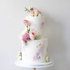 a three tiered cake decorated with pink flowers and macaroons on a white stand