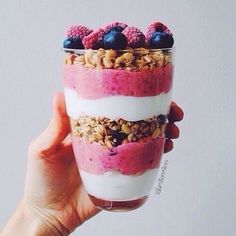 a person holding up a cup with granola and berries on top