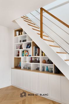 a book shelf under a stair case in a room with white walls and wooden floors