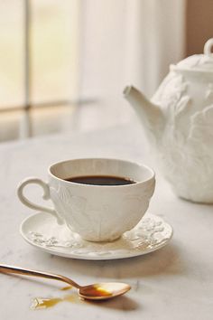 a cup of coffee sitting on top of a saucer next to a tea pot