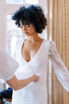 a woman in a white dress standing next to a window