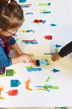 two children are painting on a table with colorful paper airplanes and arrows in the background