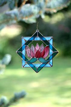 a stained glass ornament hanging from a tree branch with a pink flower in the center