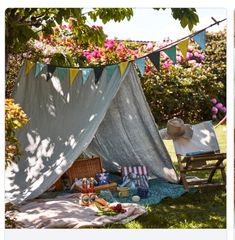 an outdoor tent with picnic food on the ground and flowers in the backgroud