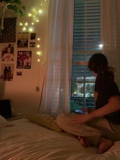 a woman sitting on top of a bed next to a window with string lights hanging from it