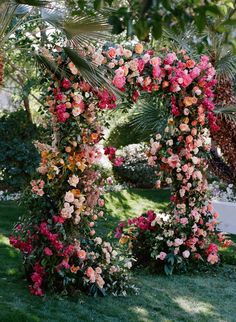 an arch made out of flowers and greenery in the middle of a lawn area