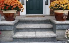 two large flower pots sitting on the steps to a front door with flowers in them