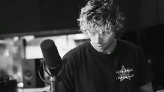 a young man sitting in front of a microphone with curly hair on his head and wearing a black t - shirt