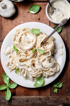 a white plate topped with pasta covered in sauce and basil leaves next to two bowls of mushrooms