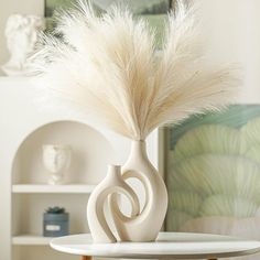 a white vase sitting on top of a table filled with flowers and feathers in it