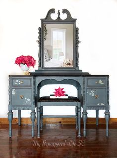 a vanity with a mirror, bench and flowers on it