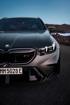 the front end of a silver bmw car on a road near some rocks and water