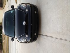 the front end of a black car parked in a driveway next to a sidewalk and house