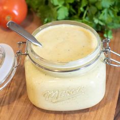 a glass jar filled with dressing sitting on top of a wooden cutting board next to tomatoes