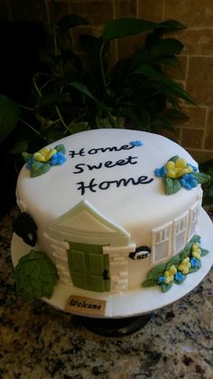 a white cake with blue and yellow flowers on it sitting on a table next to a potted plant