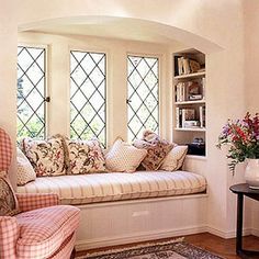 a window seat in the corner of a room with pillows on it and vases filled with flowers