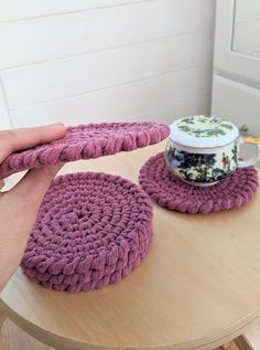 a person is holding two crocheted coasters on a table with a coffee cup