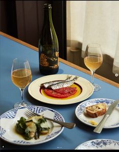 a table topped with plates and glasses of wine next to a bottle filled with liquid