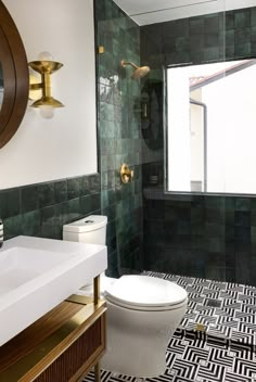 a white toilet sitting next to a bathroom sink under a mirror in a green tiled room