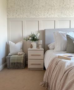 a white bed sitting next to a nightstand with flowers on top of it in a bedroom