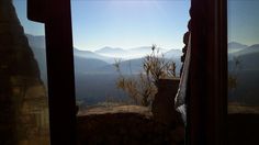 the sun is shining brightly over mountains from inside a window in a stone building with sheer curtains