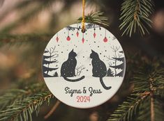 a christmas ornament hanging from a tree with two cats in the snow on it