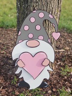 a gnome holding a heart standing next to a tree