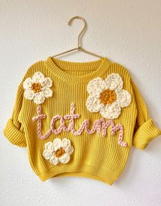 a yellow sweater with crocheted flowers and the words i am written on it