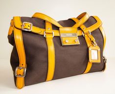 "An authentic Prada shoulder bag. The bag features a brown canvas exterior, orange leather trim, and silver-tone hardware. The interior is lined with yellow leather and there is one zipped pocket. The interior is neat & clean. The exterior is in very good condition, the trim has minor signs of use on the bottom and corners of the bag. Overall the bag is in really good condition and comes with its Prada cards and dust bag. Dimensions (cm & inch) Width: 40 cm / 15,7\" Height: 23,5 cm / 9,3\" Depth Orange Travel Bag With Silver-tone Hardware, Designer Yellow Satchel For Travel, Cognac Travel Bag With Silver-tone Hardware, Yellow Rectangular Bag With Silver-tone Hardware, Travel Bags With Palladium Hardware In Brown, Brown Coated Canvas Shoulder Bag With Palladium Hardware, Yellow Travel Shoulder Bag With Palladium Hardware, Yellow Bags With Silver-tone Hardware For Everyday Use, Brown Satchel With Silver-tone Hardware For Travel